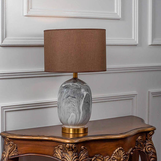 Table lamp with glass base and brown fabric shade on wooden console table warm ambient lighting for classic home decor.