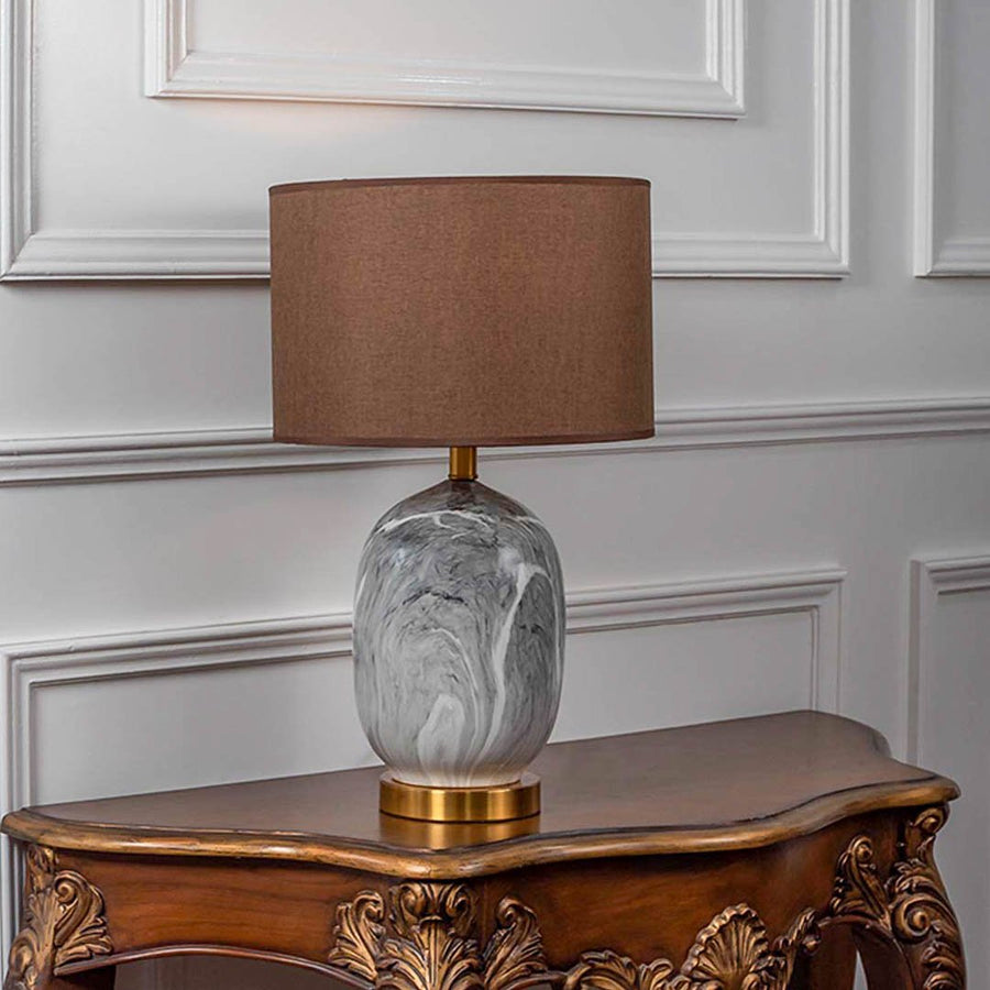 Table lamp with glass base and brown fabric shade on wooden console table warm ambient lighting for classic home decor.