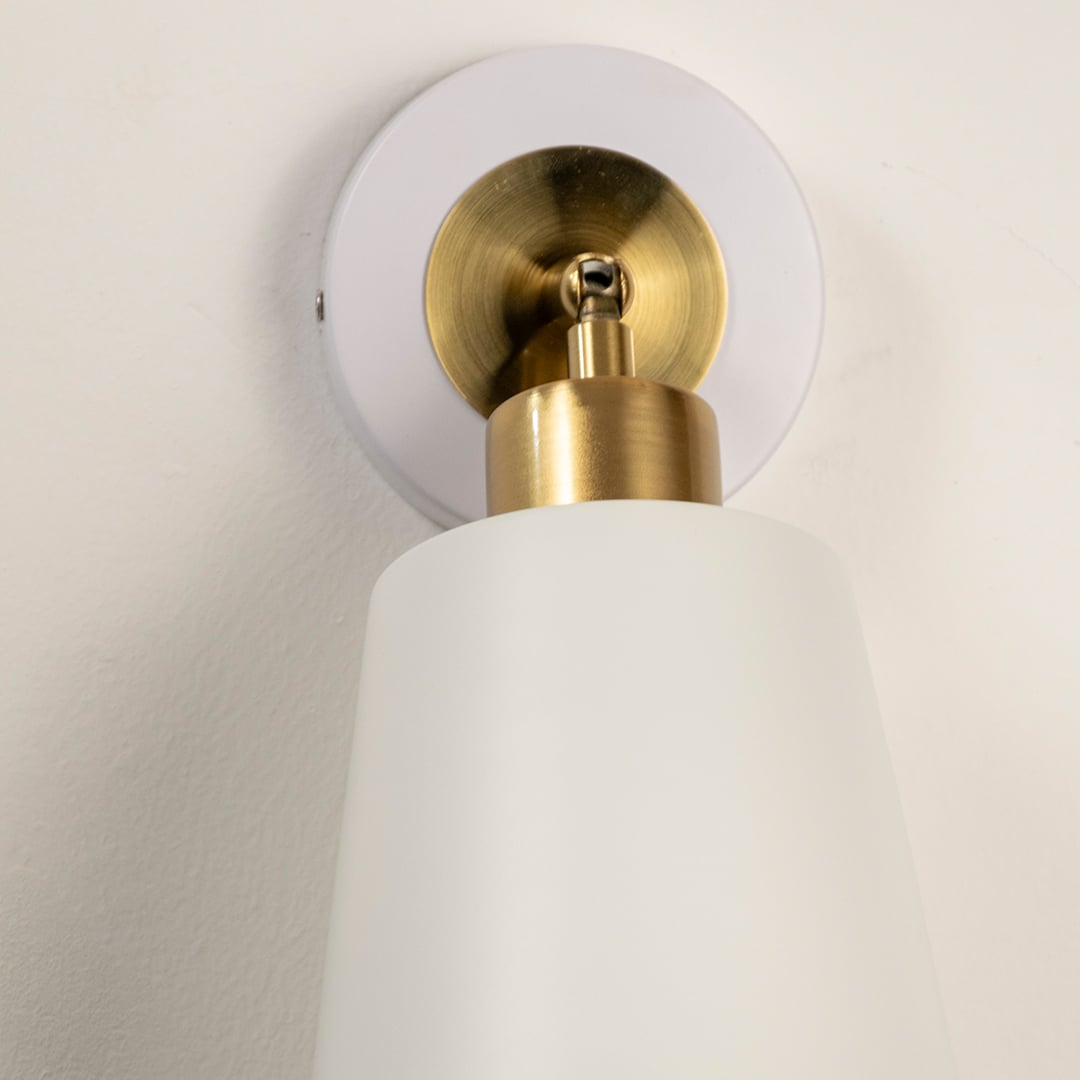 Closeup of white metal wall light with golden holder showing refined craftsmanship and smooth matte finish.