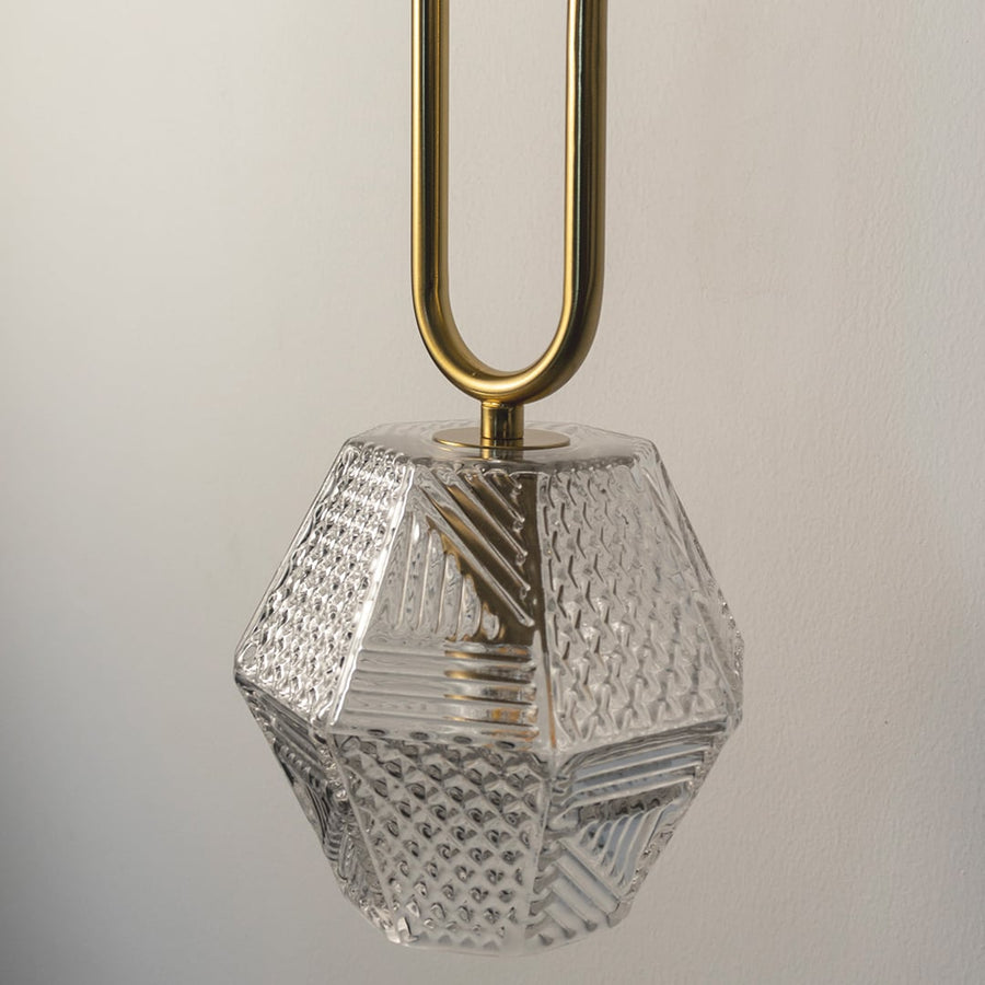Closeup of faceted clear glass pendant light with gold metal holder highlighting geometric texture premium finish and modern lighting craftsmanship.