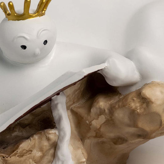 Closeup of white sculpture showing detailed parent and child reading together with golden crown design.