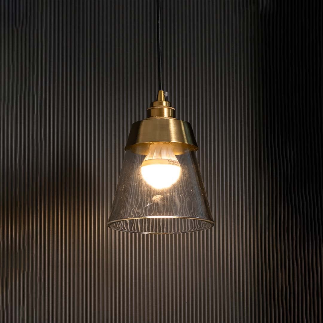 Clear cone pendant light with gold metal top glowing warmly on a dark background showcasing bright ambient light and a refined contemporary style.