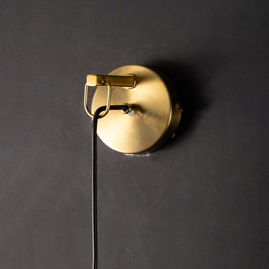 Closeup view of polished gold brass rod and clear tapered glass of modern hanging wall lamp showing high quality craftsmanship detail.