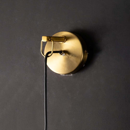 Closeup view of polished gold brass rod and clear tapered glass of modern hanging wall lamp showing high quality craftsmanship detail.