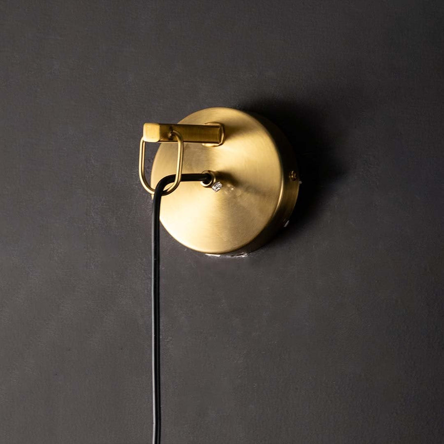 Closeup view of polished gold brass rod and clear tapered glass of modern hanging wall lamp showing high quality craftsmanship detail.