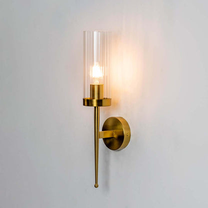 Modern brass wall light with clear glass cylinder shade creating warm elegant interior lighting decor.