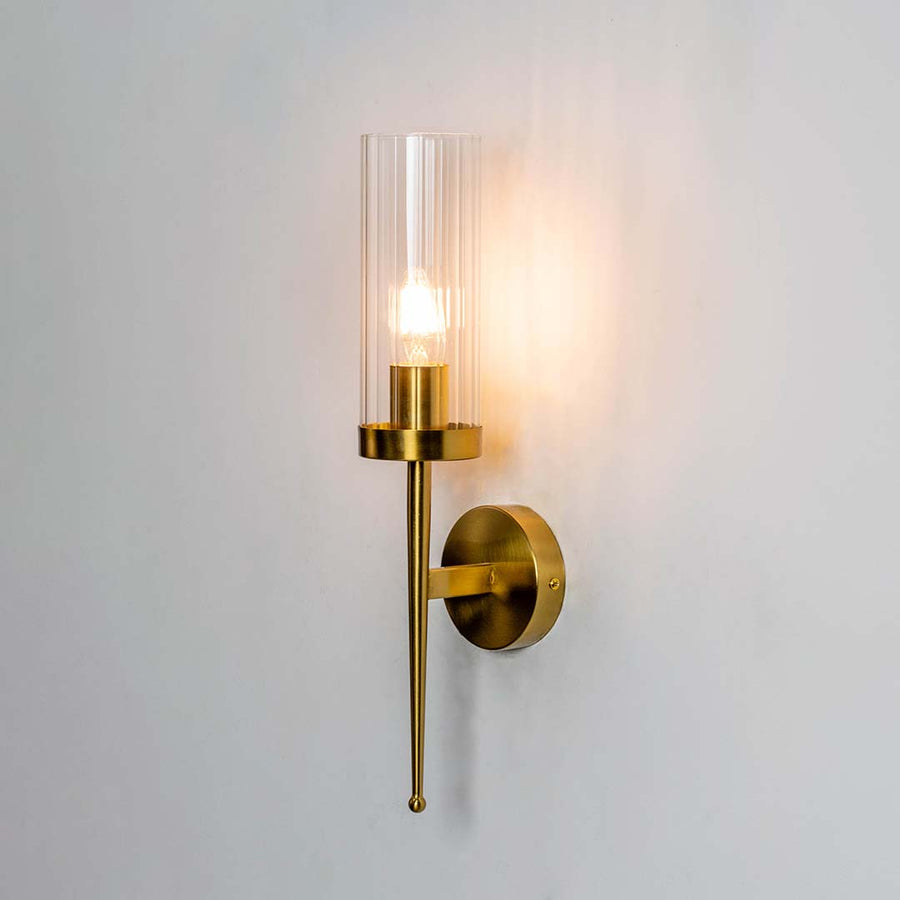 Modern brass wall light with clear glass cylinder shade creating warm elegant interior lighting decor.