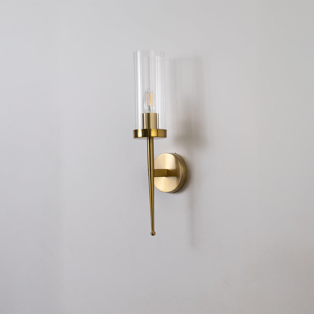 Contemporary brass wall light with sleek clear glass shade for stylish bedroom and hallway decor.