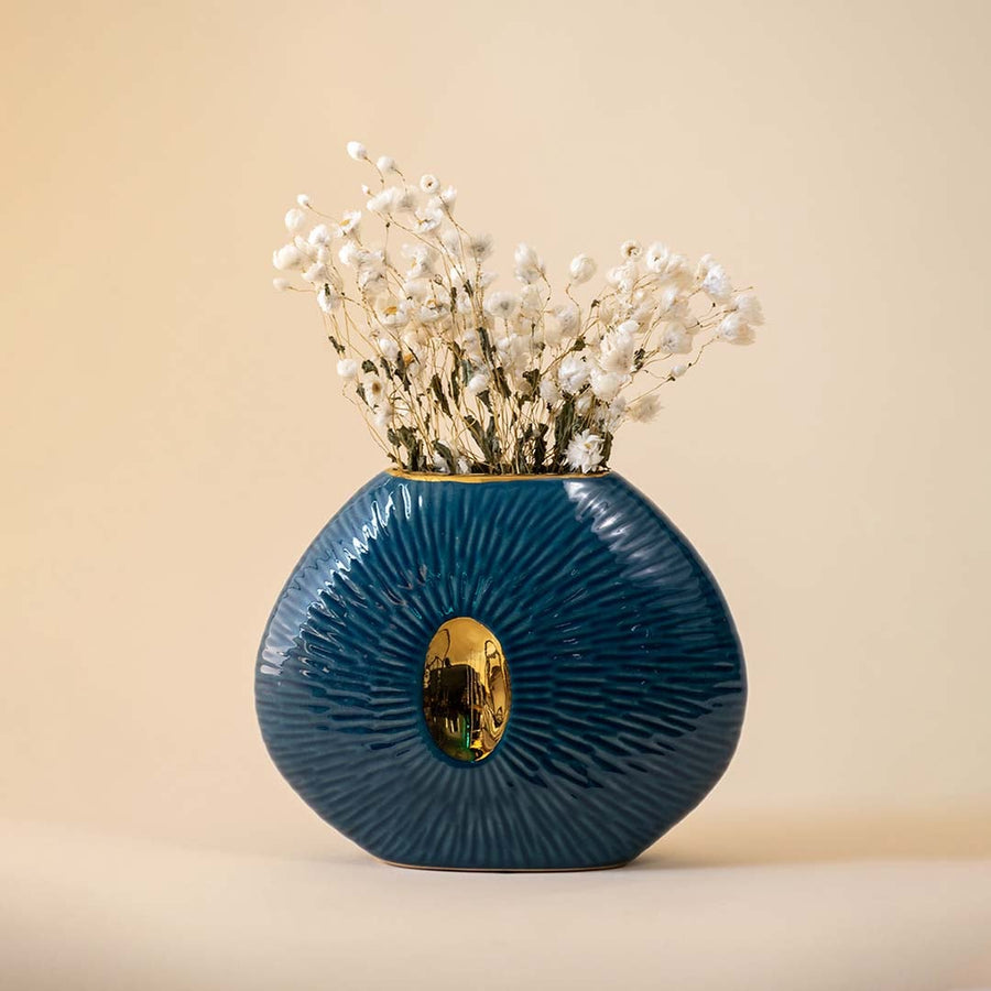 Blue oval ceramic vase with gold accent featuring ribbed texture and glossy finish displayed on beige background.