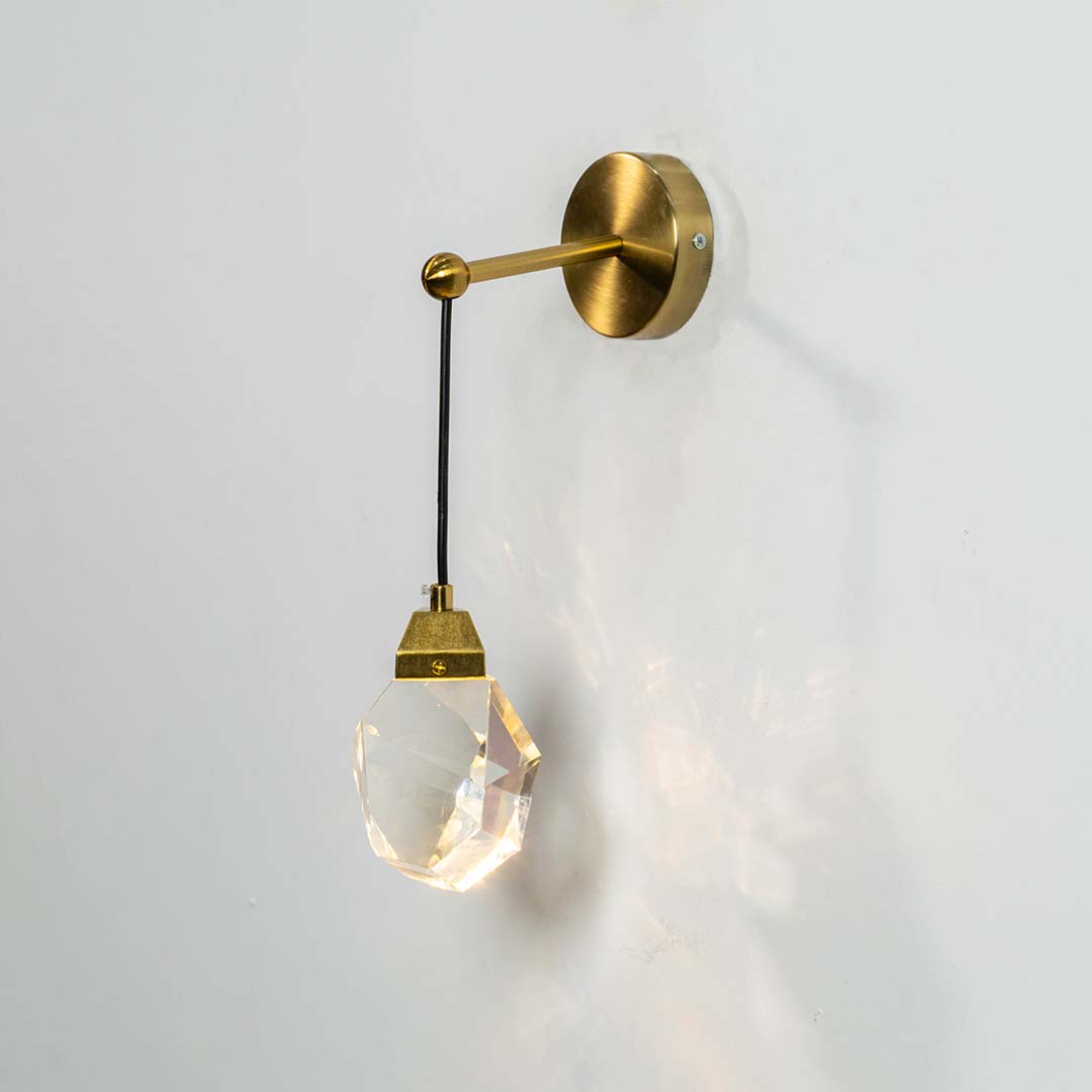 Crystal pendant light with gold metal cap switched on against a white background showing bright warm illumination and a premium faceted modern design.