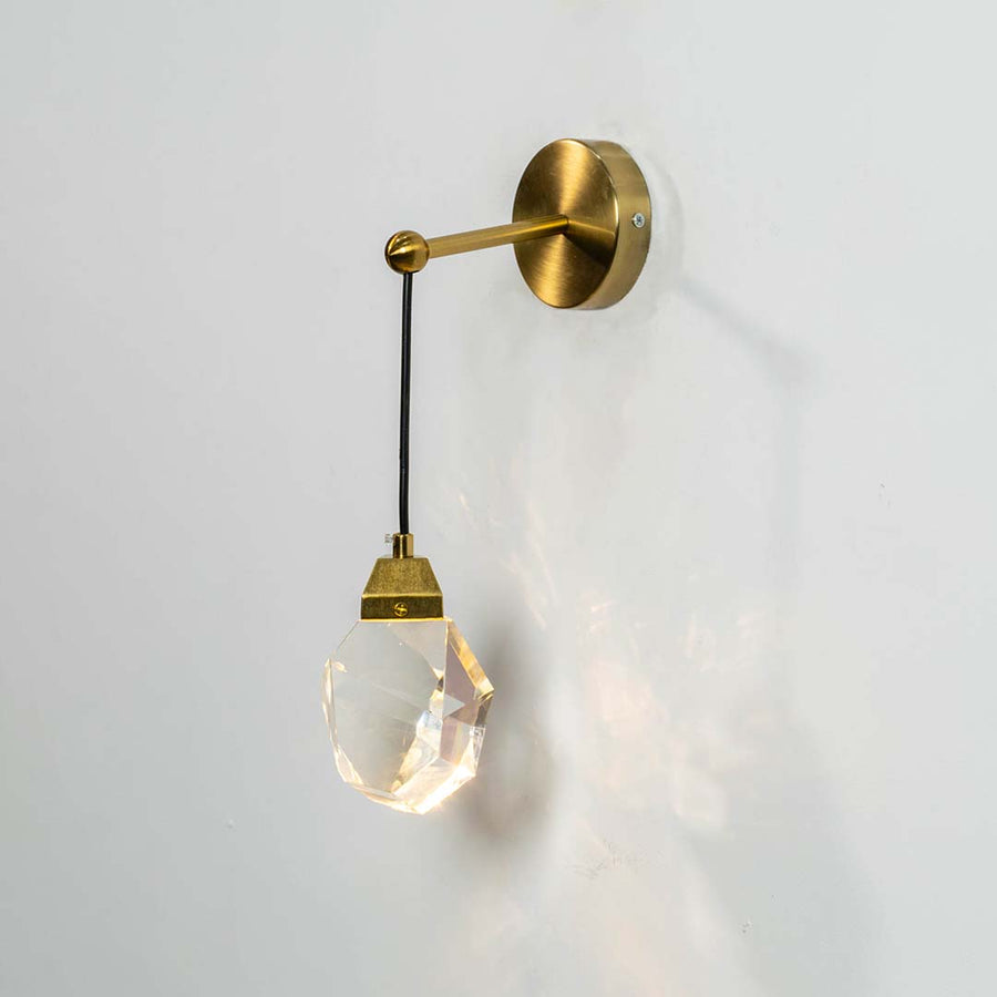 Crystal pendant light with gold metal cap switched on against a white background showing bright warm illumination and a premium faceted modern design.