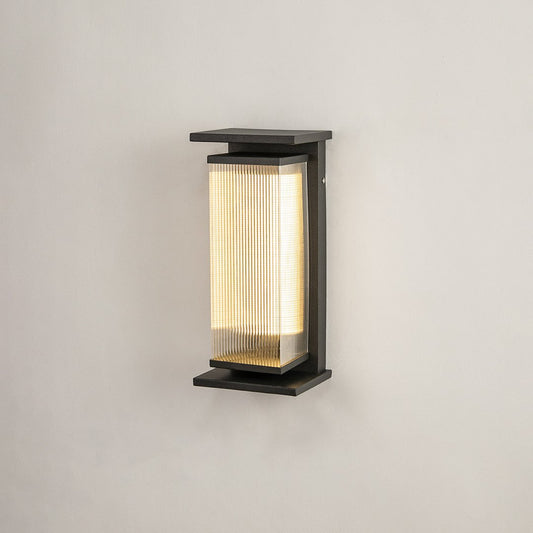 Modern black metal outdoor wall light on white background with cylindrical reeded glass shade for minimal patio decor.