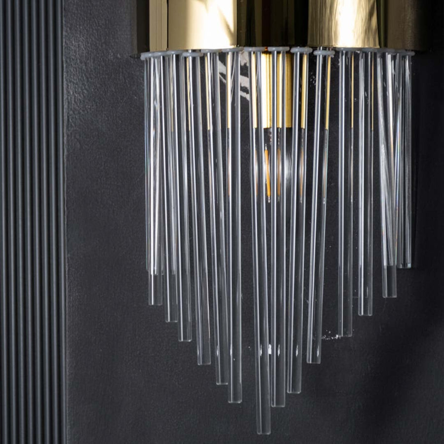 Closeup view of the wall light showing the gold band detail and glowing inner bulb shining through the layered clear glass rods.