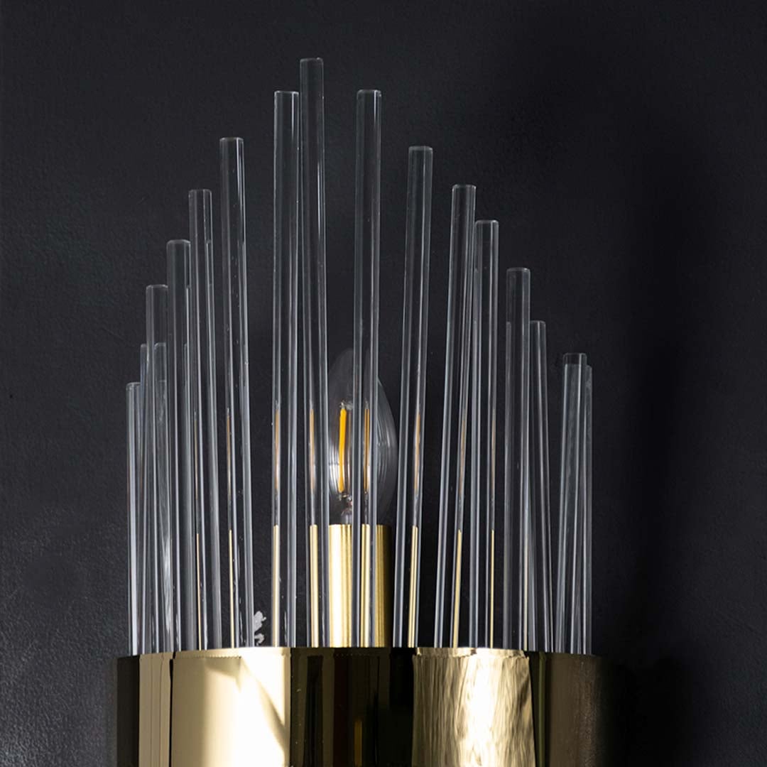 Closeup view of the wall light showing the gold band detail and glowing inner bulb shining through the layered clear glass rods.