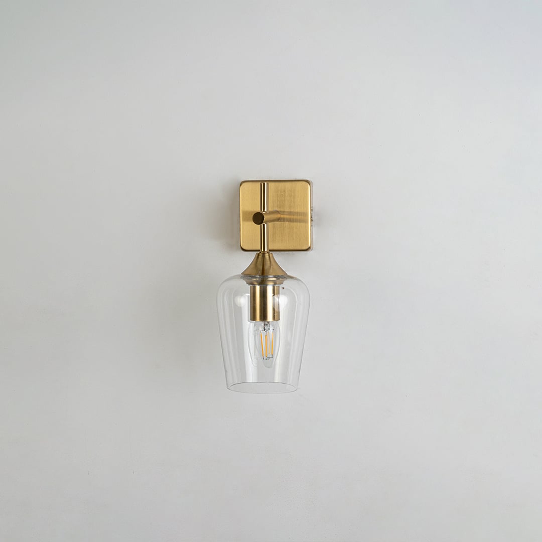 Clear glass wall light with gold metal base displayed on a white background with the light off highlighting its modern minimalist shape and premium finish.