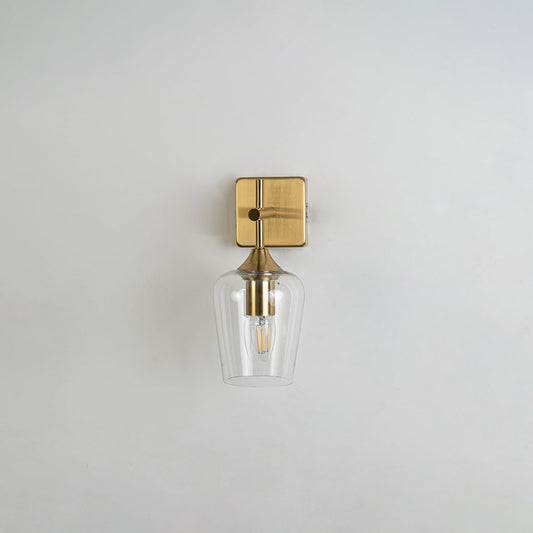 Clear glass wall light with gold metal base displayed on a white background with the light off highlighting its modern minimalist shape and premium finish.