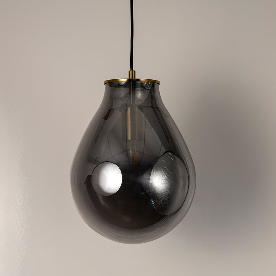 A smoked grey teardrop glass pendant light with lights off on a textured dark background emphasizing its curved tinted glass and reflective surface.