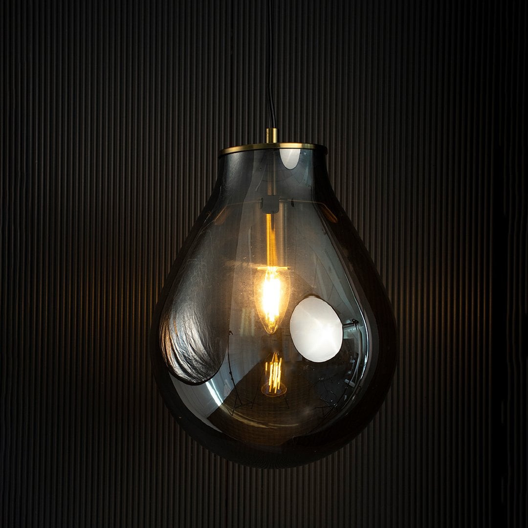 A smoked grey teardrop pendant light with lights on casting a warm glow on a dark backdrop showcasing its elegant glass silhouette and golden hardware.
