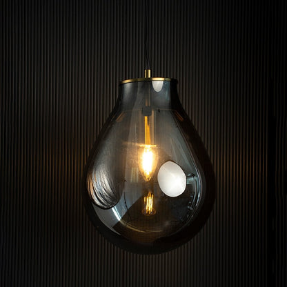 A smoked grey teardrop pendant light with lights on casting a warm glow on a dark backdrop showcasing its elegant glass silhouette and golden hardware.