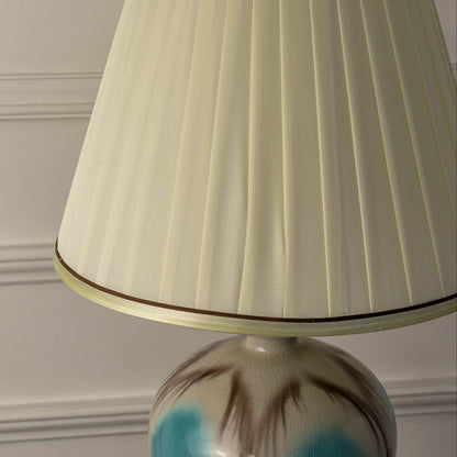 Closeup of blue ceramic table lamp featuring glossy gradient finish gold detailing and soft pleated white lampshade.