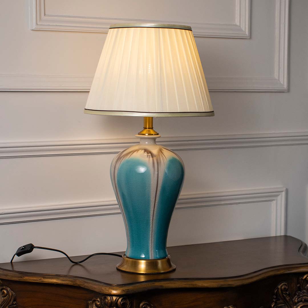 Blue ceramic table lamp with white fabric shade creating warm ambient lighting for sophisticated bedside table decor.