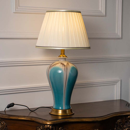 Blue ceramic table lamp with white fabric shade creating warm ambient lighting for sophisticated bedside table decor.