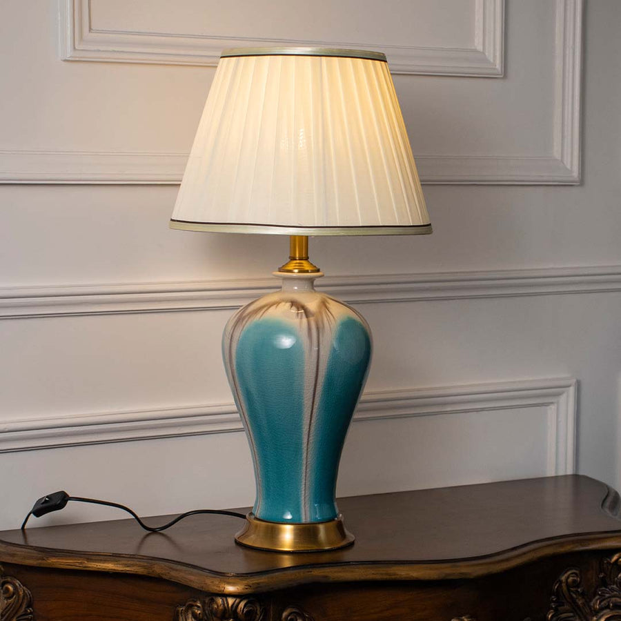 Blue ceramic table lamp with white fabric shade creating warm ambient lighting for sophisticated bedside table decor.