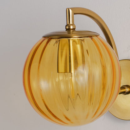 Amber glass globe wall light closeup highlighting ribbed texture and gold metal arm detail for vintage inspired interior lighting decor.