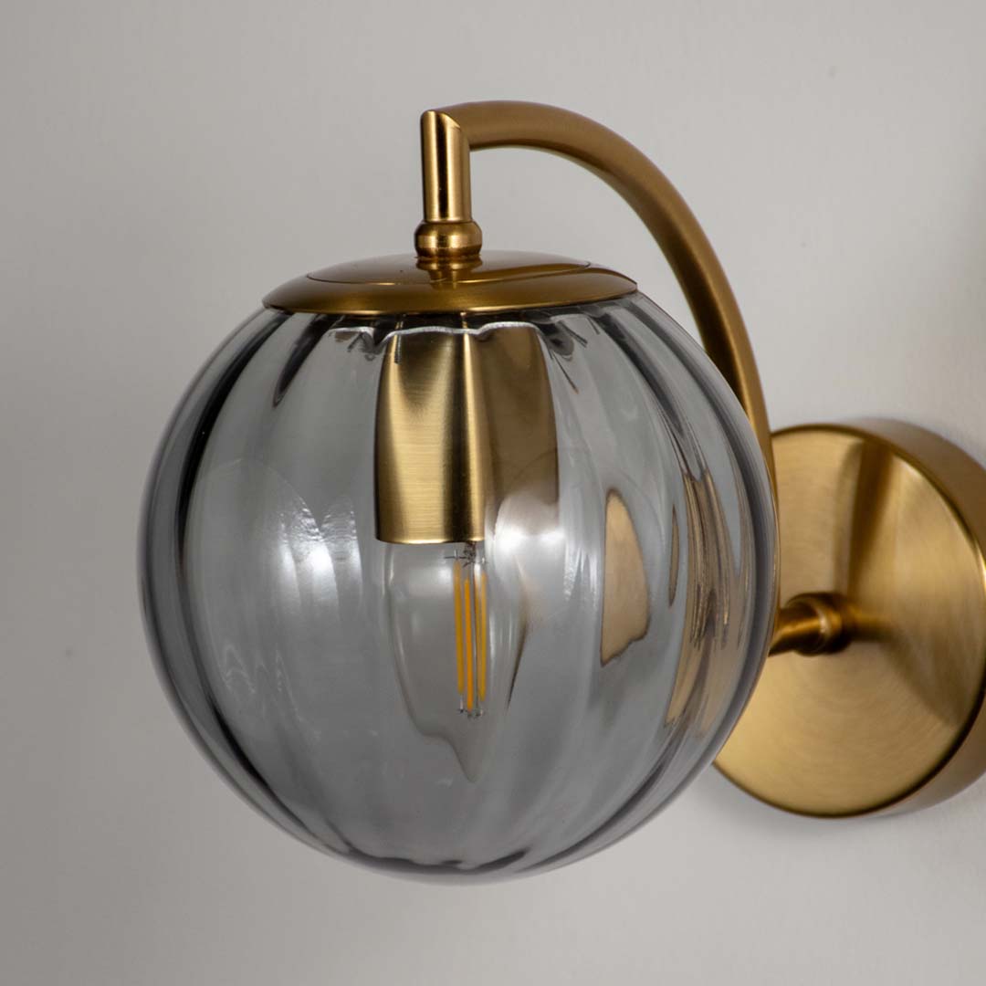 Closeup of smoked glass and gold metal wall light for modern bedroom and premium decor styling spaces.
