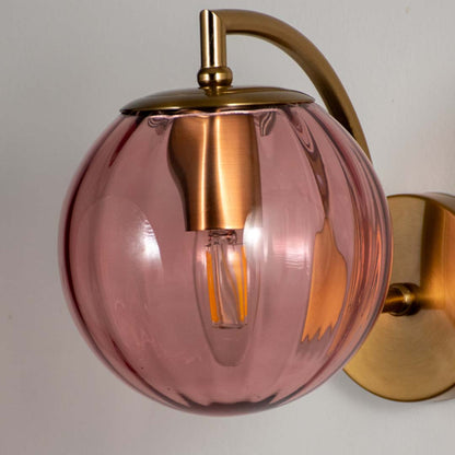 Decorative smoked pink glass wall light with gold metal base mounted on neutral wall background ideal for luxury interior lighting setup.
