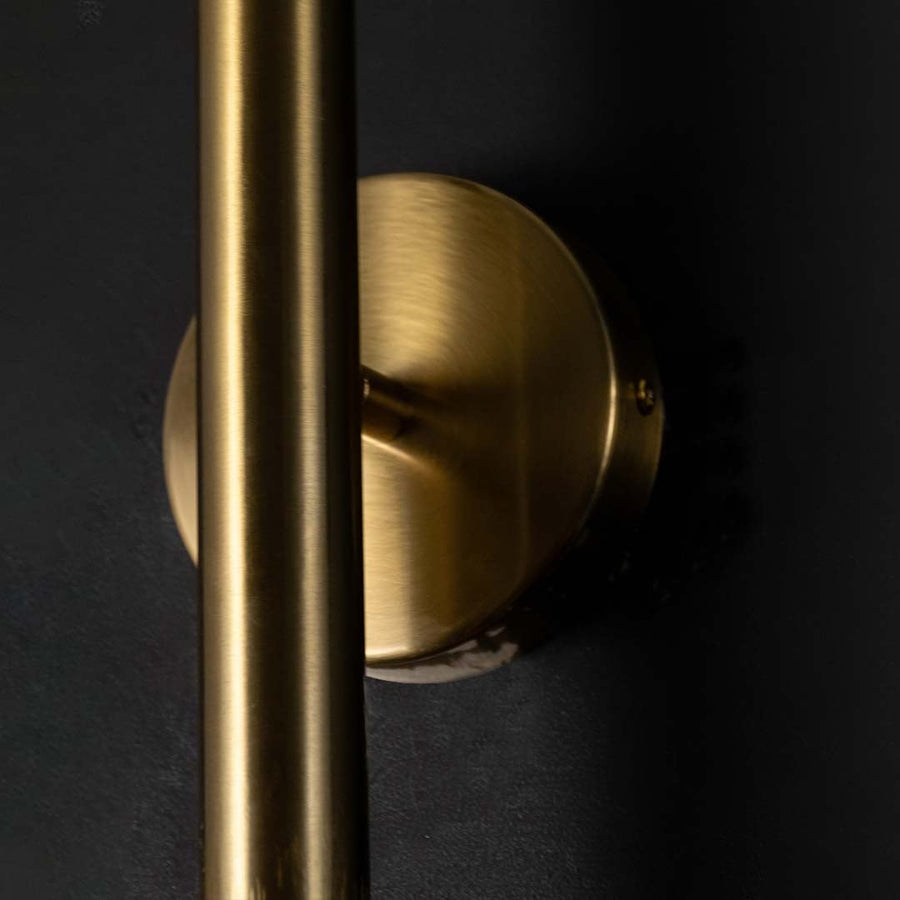 Detailed closeup of gold metal wall light highlighting its slim cylindrical structure and clear bulb form for refined modern decorative lighting.