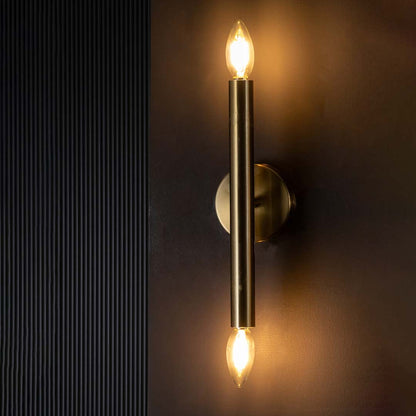 Gold double ended wall light glowing warmly on a dark background showcasing its sleek metal tube and bright ambient vertical lighting effect.