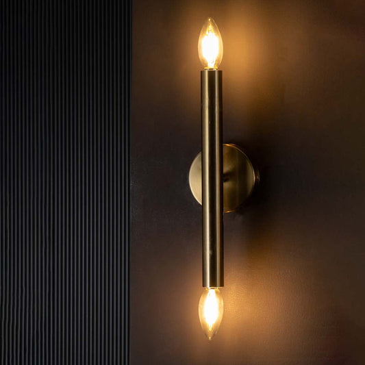 Gold double ended wall light glowing warmly on a dark background showcasing its sleek metal tube and bright ambient vertical lighting effect.