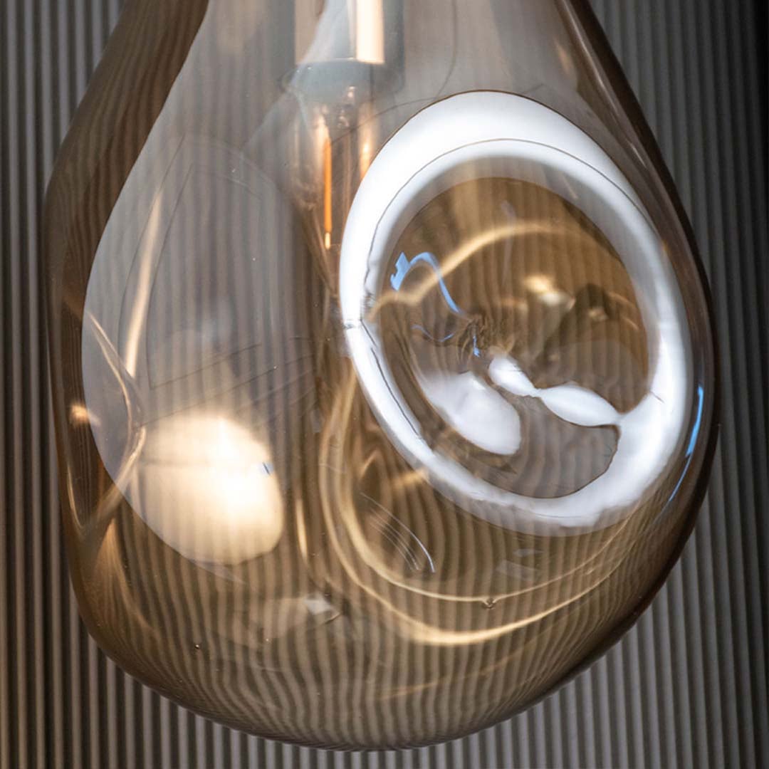 Closeup view of amber glass pendant showing warm illuminated bulb and reflective curved glass surface adding modern elegance.