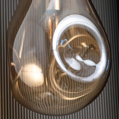 Closeup view of amber glass pendant showing warm illuminated bulb and reflective curved glass surface adding modern elegance.