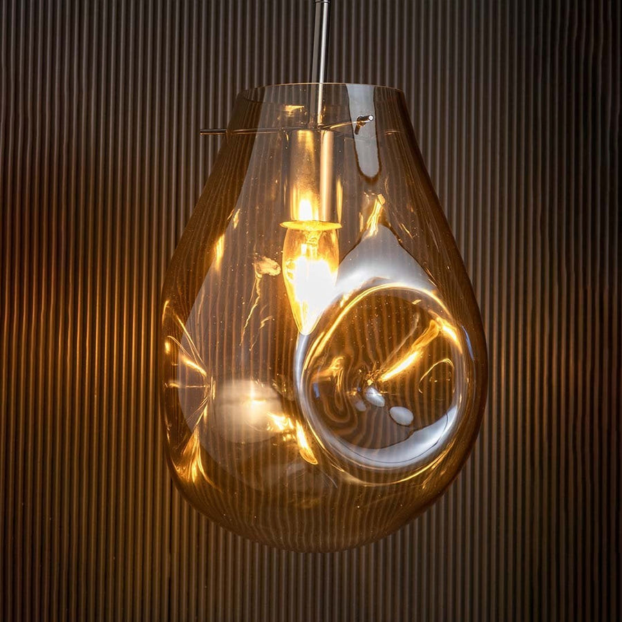 Amber glass pendant light on against a dark black background highlighting its warm illuminated glow and reflective glass finish.