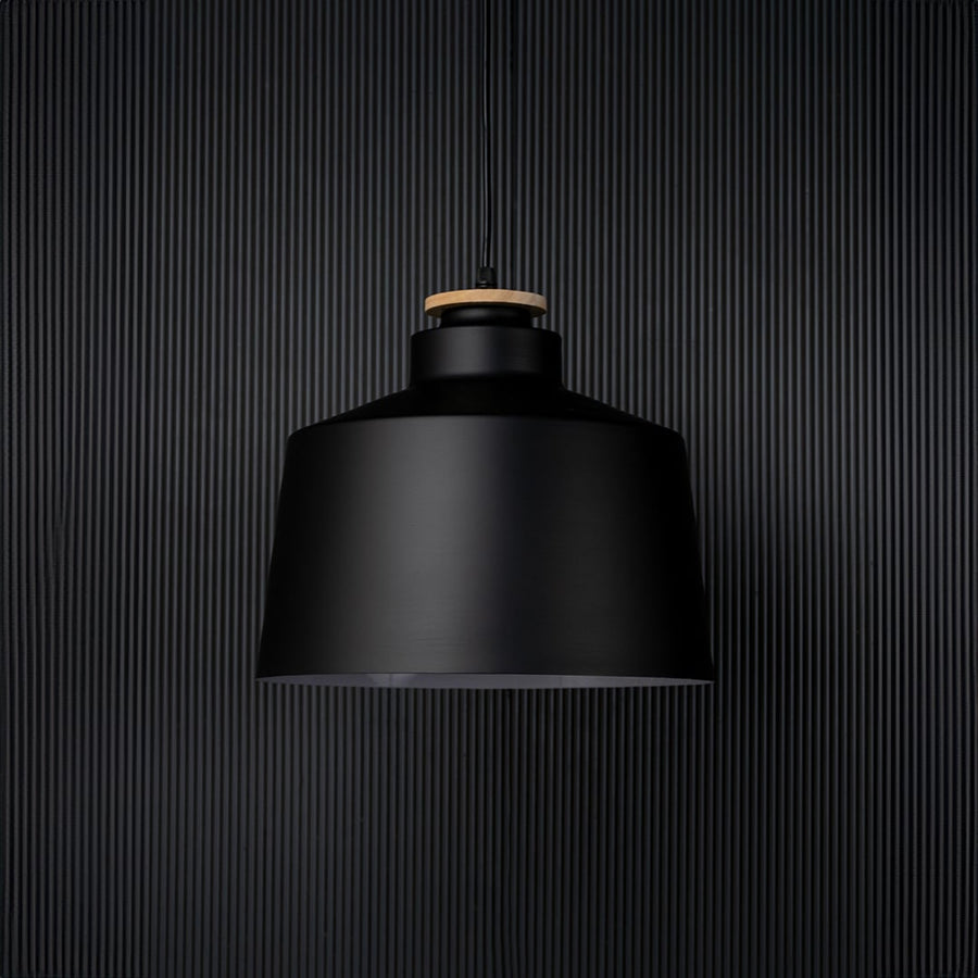 A contemporary black pendant light captured on a black background with the light off emphasising its bold structure and sleek matte finish in a minimalist setting.