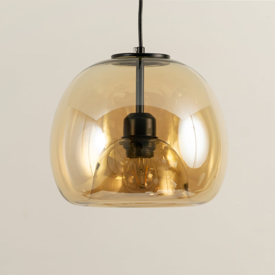 Closeup of amber glass pendant light revealing warm bulb glow and smooth curved shade with black metal detailing for elegant interior lighting.