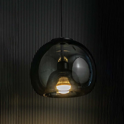 Smoked glass pendant light illuminated against a dark textured background  highlighting its reflective dome shape.