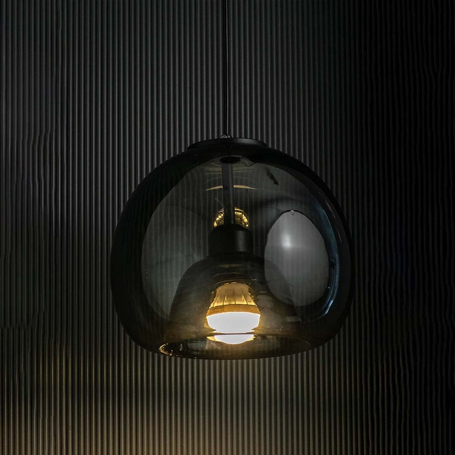 Smoked glass pendant light illuminated against a dark textured background  highlighting its reflective dome shape.