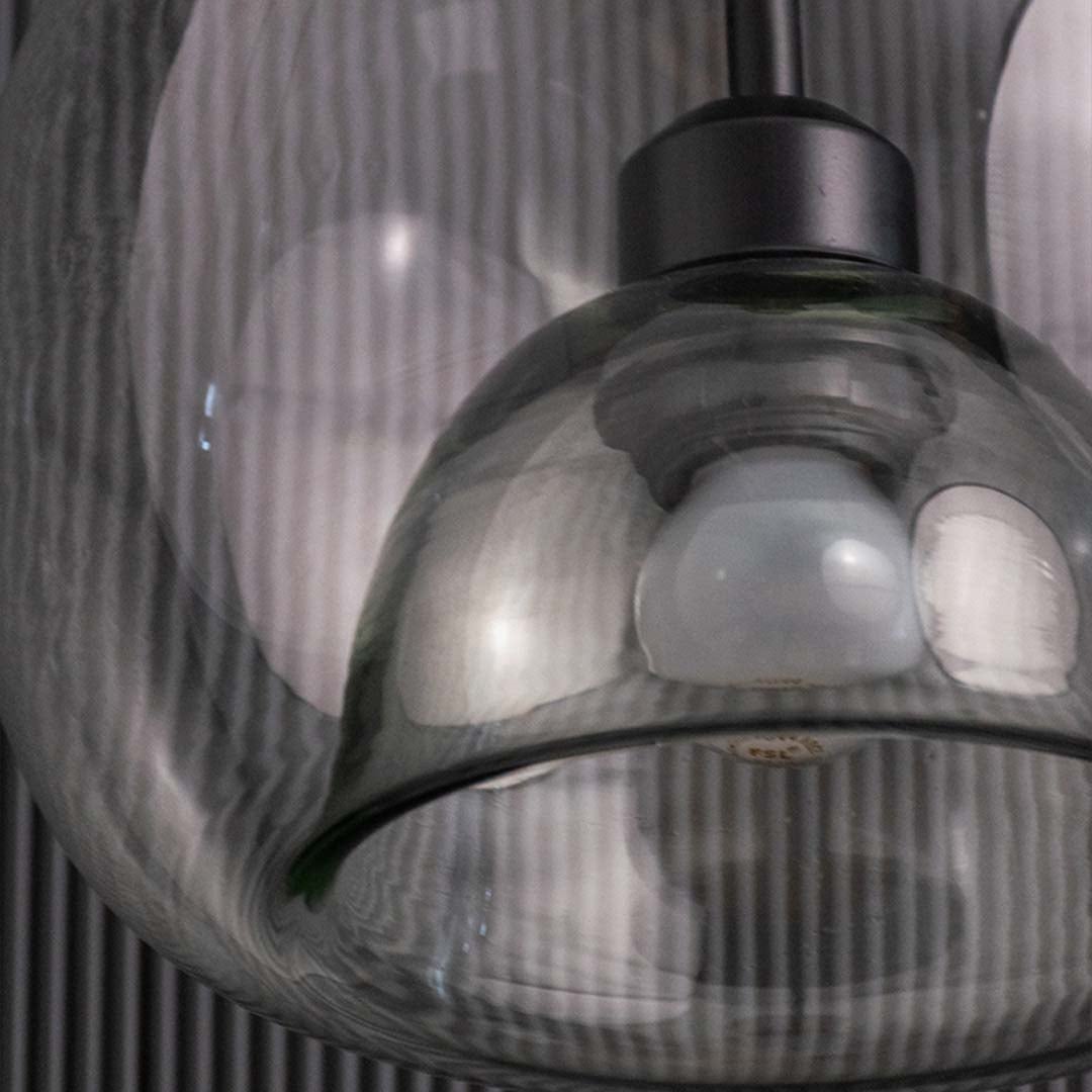 Closeup table lamp with layered clear glass dome design showing bulb on a deep black textured backdrop.