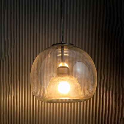 Table lamp with a clear glass dome pendant glowing softly against a dark textured background.