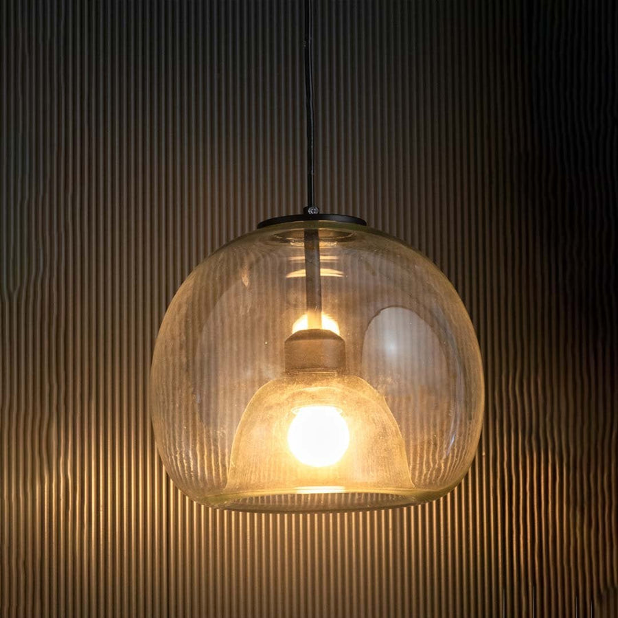 Table lamp with a clear glass dome pendant glowing softly against a dark textured background.
