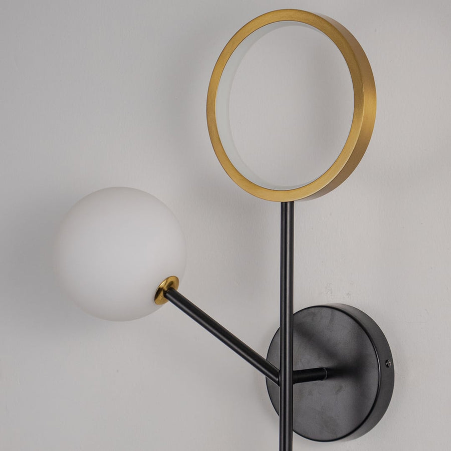Contemporary black wall lamp with golden ring and frosted glass globe ideal for bedroom or living room decor.