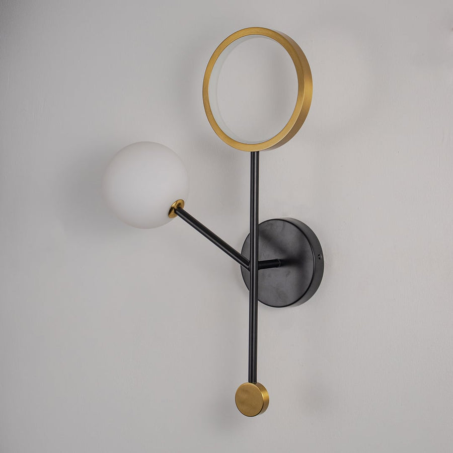 Modern black and gold wall light with white glass globe shade displayed on plain white wall.