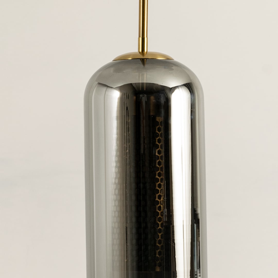 Closeup of smoked grey cylindrical glass pendant with gold fitting and warm mesh diffuser showcasing its refined modern craftsmanship.