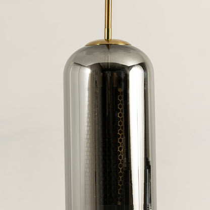 Closeup of smoked grey cylindrical glass pendant with gold fitting and warm mesh diffuser showcasing its refined modern craftsmanship.