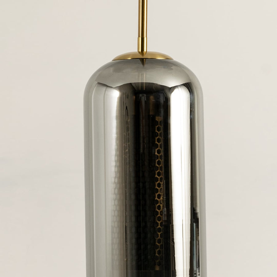 Closeup of smoked grey cylindrical glass pendant with gold fitting and warm mesh diffuser showcasing its refined modern craftsmanship.