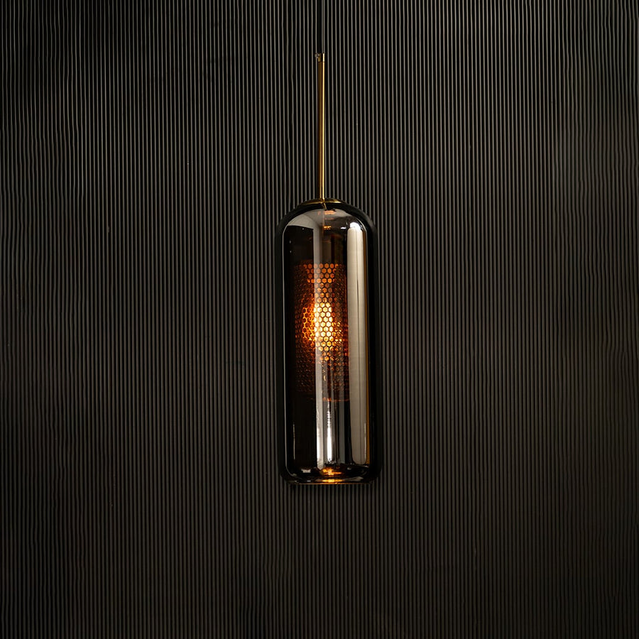 Tall smoked grey glass pendant with gold fitting and warm glowing diffuser highlighted on a dark background creating a dramatic stylish lighting accent.