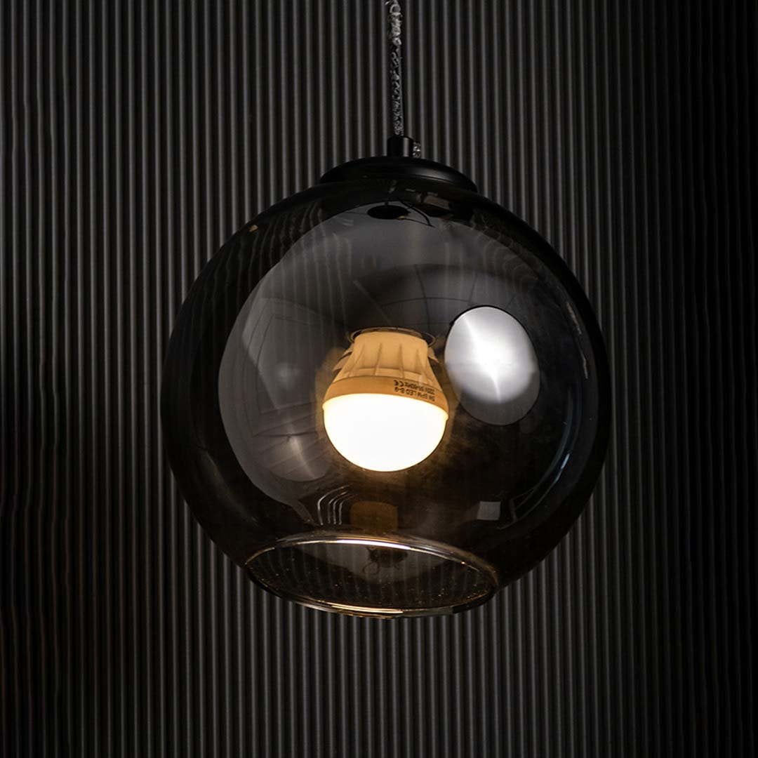 Smoked black glass globe pendant with warm glowing filament bulb highlighted on a dark background creating a dramatic stylish lighting accent.